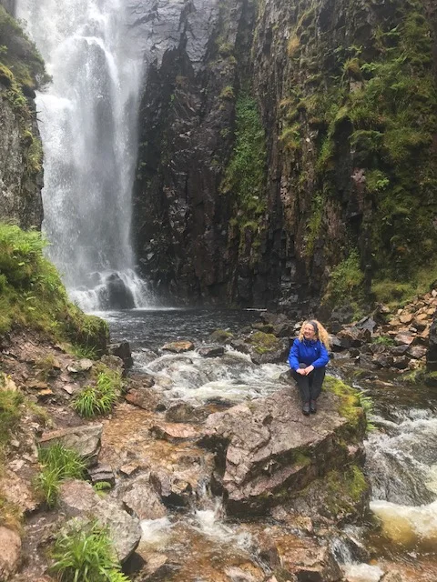Lynn sitting beside a waterfall in Scotland