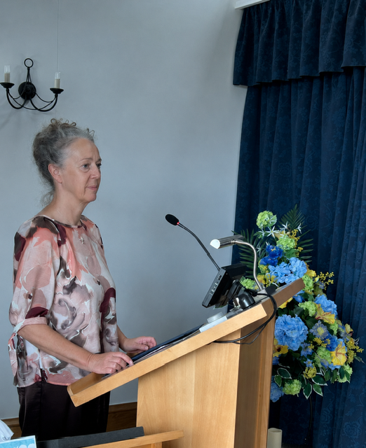 Lynn standing at a lectern beside flowers